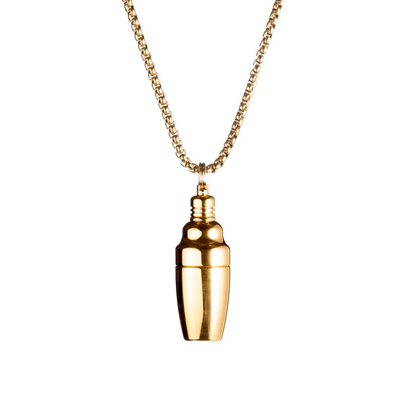 May include: A gold-colored necklace featuring a pendant shaped like a cocktail shaker. The pendant is a shiny, metallic gold and hangs from a delicate gold chain. The background is plain white.