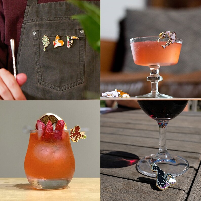 Puede incluir: Un conjunto de pines de esmalte con varios dise&ntilde;os, incluyendo un tuc&aacute;n, un zorro, un pulpo, un gato y una sirena. Los pines se muestran en una chaqueta vaquera, una mesa de madera y una copa de vino tinto.