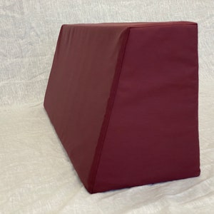 May include: A burgundy wedge pillow with a zippered cover. The pillow is made of a soft, comfortable fabric and is designed to provide support and comfort.