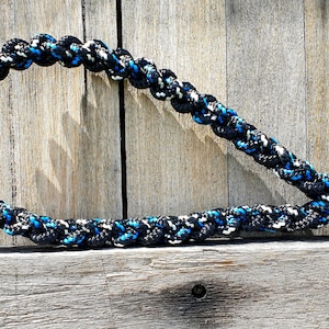 Puede incluir: Un juguete para perros de cuerda trenzada de color negro, azul y blanco con un extremo anudado.