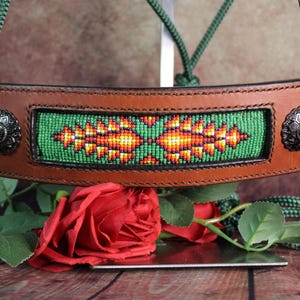 May include: A brown leather horse halter with a green beaded design. The halter features a green rope and decorative silver-toned metal accents. The central panel has a vibrant green background with an orange and yellow geometric pattern.