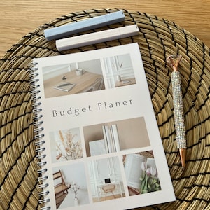 Könnte beinhalten: Ein weißer Spiralblock-Budgetplaner mit dem Text "Budget Planner" auf dem Cover. Das Cover zeigt Fotos von einem Schreibtisch, einer Vase mit Trockenblumen, einem Buch und einem Stuhl.