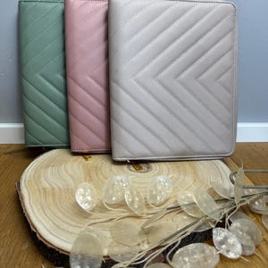 Könnte beinhalten: Drei Reißverschlusstaschen in verschiedenen Farben: Salbeigrün, Staubrosa und Hellgrau. Die Taschen haben ein gestepptes Chevron-Muster und sind aus einem weichen, strukturierten Material gefertigt.