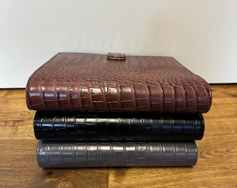Op de afbeelding: Een stapel van drie organizers van imitatieleer met een krokodillenleertextuur. De bovenste organizer is bruin, de middelste is zwart en de onderste is grijs. De bruine organizer heeft een kleine, ronde sluiting.