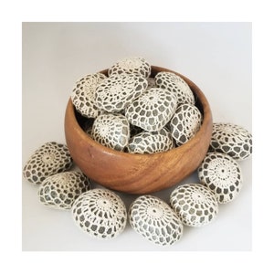 May include: A wooden bowl filled with smooth gray stones covered in white crocheted lace. Several additional stones are scattered around the bowl.