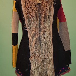 Könnte beinhalten: Ein schwarzer, brauner, gelber und roter Patchwork-Cardigan mit einem langen, braunen Kunstfellkragen. Der Cardigan hat einen gewellten Saum mit bunten Punkten.