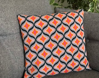 Puede incluir: Una almohada decorativa con un patrón geométrico en tonos de rosa, naranja y negro. La almohada está en un sofá gris.