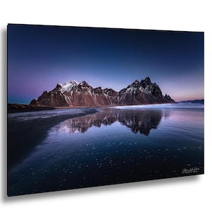 Puede incluir: Fotografía de paisaje de una cordillera reflejada en el agua al anochecer. Las montañas son de color marrón oscuro con picos nevados. El agua es de color azul oscuro y el cielo pasa del azul oscuro al púrpura.