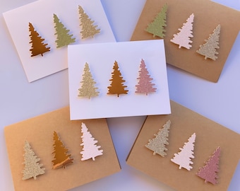 May include: A selection of Christmas cards with glittery tree decorations in gold, bronze, pink, and green. The cards are on white and brown cardstock, perfect for the festive season.