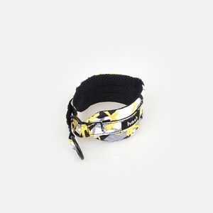 Puede incluir: Un collar para perros con un estampado de camuflaje en amarillo, gris y blanco. El collar tiene un interior de malla negra y un anillo de metal negro. La palabra "hash" est&aacute; impresa en el collar.