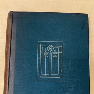 Può includere: Un libro con copertina rigida blu-verde e dorso marrone. La copertina presenta un disegno geometrico dorato. Il libro è chiuso e sembra in buone condizioni, con una leggera usura sui bordi.
