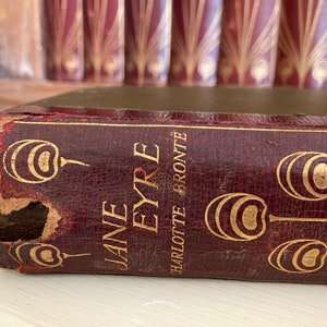 Può includere: Un libro vintage rilegato in pelle rossa con lettere dorate e accenti decorativi. Il titolo è "Jane Eyre" di Charlotte Brontë.