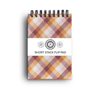May include: A small notepad with a plaid pattern in shades of orange, pink, and brown. The notepad has a black wire binding and a white label that reads "SHORT STACK FLIP PAD".