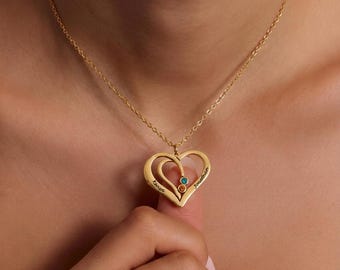 Op de afbeelding: Een goudkleurige ketting met een dubbele hartvormige hanger. De hanger is gegraveerd met de namen Kenya en Jonathan en is versierd met twee kleine ronde edelstenen, een blauwe en een oranje, gezet in de hartstructuur.