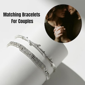 Op de afbeelding: Twee zilverkleurige armbanden, één met een gestructureerde staaf met houtnerfpatroon en een schakelketting, en de andere ontworpen als een slanke tak met kleine zijtakjes. De afbeelding bevat de tekst Matching Bracelets For Couples.