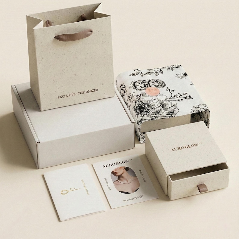 May include: Gift packaging set in light beige, including a paper bag with a brown handle, a white box, a floral-printed box, and a small drawer box. The bag has the text "EXCLUSIVE - CUSTOMIZED".