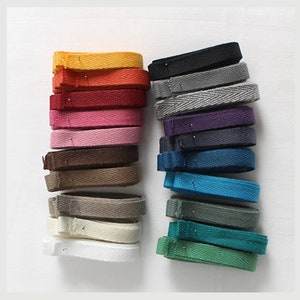 May include: A collection of 20 cotton twill ribbon in various colours, including yellow, orange, red, pink, brown, grey, white, black, blue, and green. The ribbon is arranged in two stacks, with each stack containing 10 ribbons.