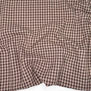 May include: Close-up of a fabric featuring a brown and beige gingham pattern. The fabric is draped, creating soft folds and shadows. The checkered design is evenly spaced, giving a classic, rustic appearance.