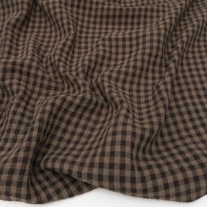 May include: A close-up shot of a brown and black checked fabric. The material is draped, showing a soft texture. The pattern is a classic gingham design, with evenly spaced squares.