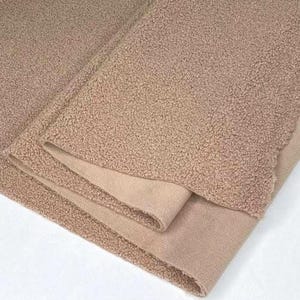 May include: Close-up of a folded, tan-colored blanket. The blanket has a textured, plush exterior and a smooth, suede-like interior. The layers are neatly folded, showcasing the contrast in textures and tones.