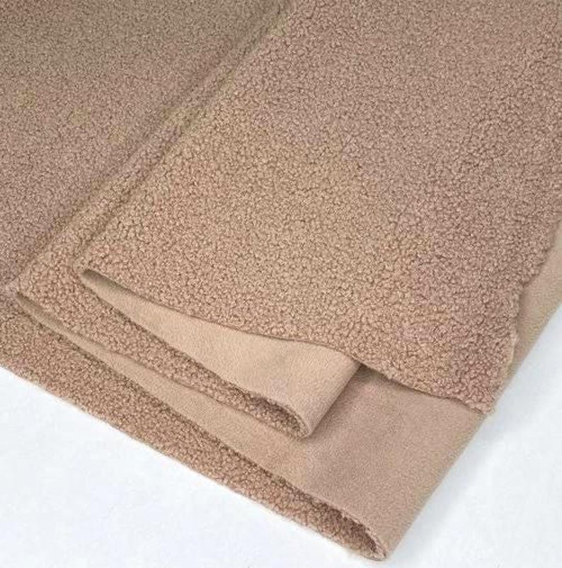 May include: Close-up of a folded, tan-colored blanket. The blanket has a textured, plush exterior and a smooth, suede-like interior. The layers are neatly folded, showcasing the contrast in textures and tones.