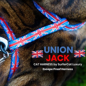 May include: A blue and red cat harness with a Union Jack pattern. The harness is escape proof and has a silver clip. The text "UNION JACK" is printed on the harness, along with the words "CAT HARNESS by SurferCat Luxury Escape Proof Harness".