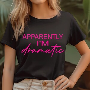 Könnte beinhalten: Schwarzes T-Shirt mit dem Text "Apparently I'm Dramatic" in rosa Schrift.