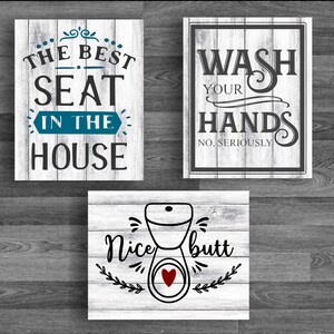 Puede incluir: Tres letreros de madera blanca con letras negras e ilustraciones. El primer letrero dice "The Best Seat in the House". El segundo letrero dice "Wash Your Hands No, Seriously". El tercer letrero dice "Nice Butt" con una ilustración de un inodoro y un corazón rojo.