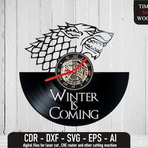 Puede incluir: Reloj de vinilo negro con una silueta blanca de un lobo huargo y las palabras "Winter is Coming". La esfera del reloj es un engranaje circular con números romanos.