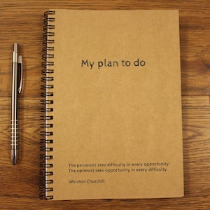 Peut inclure: Un carnet à spirales marron avec le texte "My plan to do" sur la couverture. La citation "The pessimist sees difficulty in every opportunity. The optimist sees opportunity in every difficulty. Winston Churchill" est imprimée en bas de la couverture.