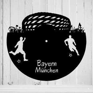 May include: Black and white silhouette of two soccer players with a soccer ball in front of a soccer goal. The text "Bayern M&uuml;nchen" is written below the players.