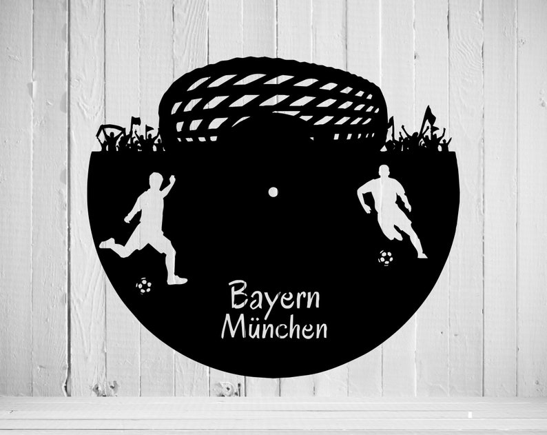 May include: Black and white silhouette of two soccer players with a soccer ball in front of a soccer goal. The text "Bayern M&uuml;nchen" is written below the players.