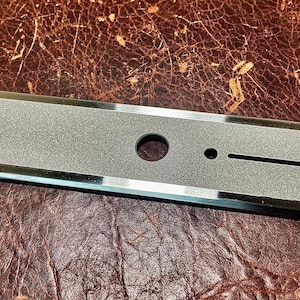 May include: A silver-colored guitar control plate with a textured surface and three holes. The plate is oval-shaped and has a raised edge.