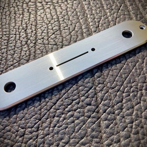Könnte beinhalten: Eine silberne Gitarren-Kontrollplatte aus Metall mit drei Löchern und einem langen, schmalen Schlitz.