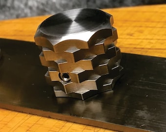 May include: A silver metal knob with a hexagonal shape and a smooth, polished finish. The knob has a small hole in the center.
