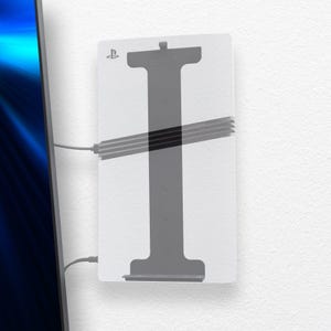 Może przedstawiać: Biały uchwyt ścienny do konsoli do gier, z szarym wzorem w kształcie litery I i symbolem PlayStation. Uchwyt ma poziome pręty i jest połączony z urządzeniem za pomocą kabla.