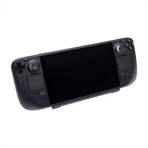 May include: A black handheld gaming device with a large screen, two joysticks, and a variety of buttons. The device has a "STEAM" button on the left side and a circular button with a small knob on the right side.