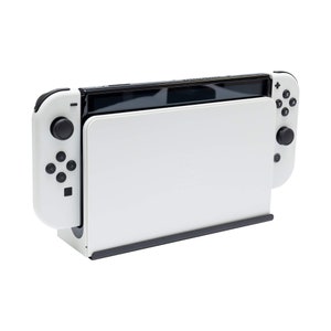 May include: A white Nintendo Switch console with black buttons and a black screen. The console is in a stand and the Joy-Con controllers are attached.