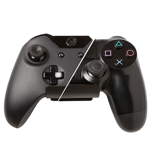 Może przedstawiać: Czarny kontroler Xbox i czarny kontroler Playstation są zamontowane razem na czarnym stojaku. Kontrolery są skierowane do siebie.