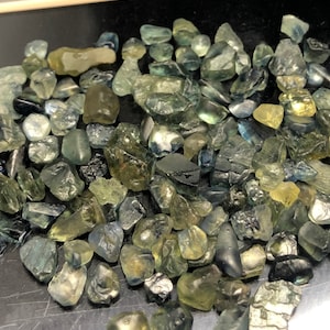 Puede incluir: Una colección de piedras preciosas verdes y azules sin pulir. Las piedras son de varios tamaños y formas, algunas tienen una apariencia más opaca que otras.