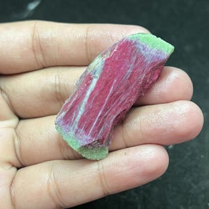 May include: A rough, raw, pink and green gemstone with a layered, striated texture.