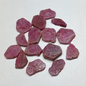 Puede incluir: Un conjunto de gemas de rubí en bruto, sin cortar. Las piedras varían en tamaño y forma, mostrando un tono rojo-rosado intenso. La apariencia natural y sin pulir de los rubíes es evidente, con texturas e imperfecciones visibles. Adecuado para joyería o coleccionismo.