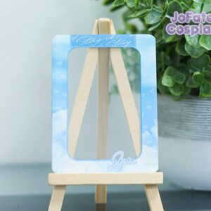 May include: A blue and white photo card with a white frame and the text "Stay in Stay" at the top and "Jeju" at the bottom. The card is on a small wooden easel.