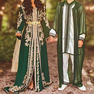 Può includere: Una coppia vestita con abiti tradizionali marocchini da matrimonio. La donna indossa un lungo abito verde con ricami dorati e una cintura dorata. L'uomo indossa una camicia bianca con una tunica verde sopra. Si tengono per mano e sorridono.