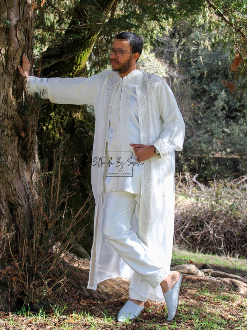 May include: A white, embroidered outfit consisting of a long coat, a tunic, and pants. The outfit features intricate detailing along the edges and sleeves. The ensemble is paired with matching white slippers. The text "Sottouch By Sophie" is visible.