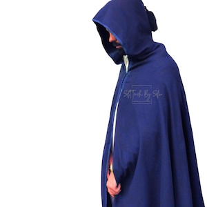 May include: A hooded cape in a deep navy blue color. The cape has a long, flowing design with a hood and a front closure. The text "Soft Touch By Sofia" is visible on the right side of the cape. The cape is made of a soft material.