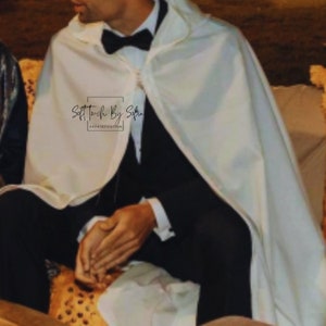 May include: A person wearing a white cape over a black suit with a black bow tie. The cape has the text "Soft Touch By Sofia Sophistication" printed on it.