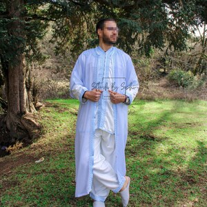 May include: A light blue robe with intricate embroidery and a matching white outfit. The robe features detailed light blue trim and embroidery along the edges. The outfit includes a long-sleeved top and loose-fitting pants. The text "Softouch By Sophie" is visible.