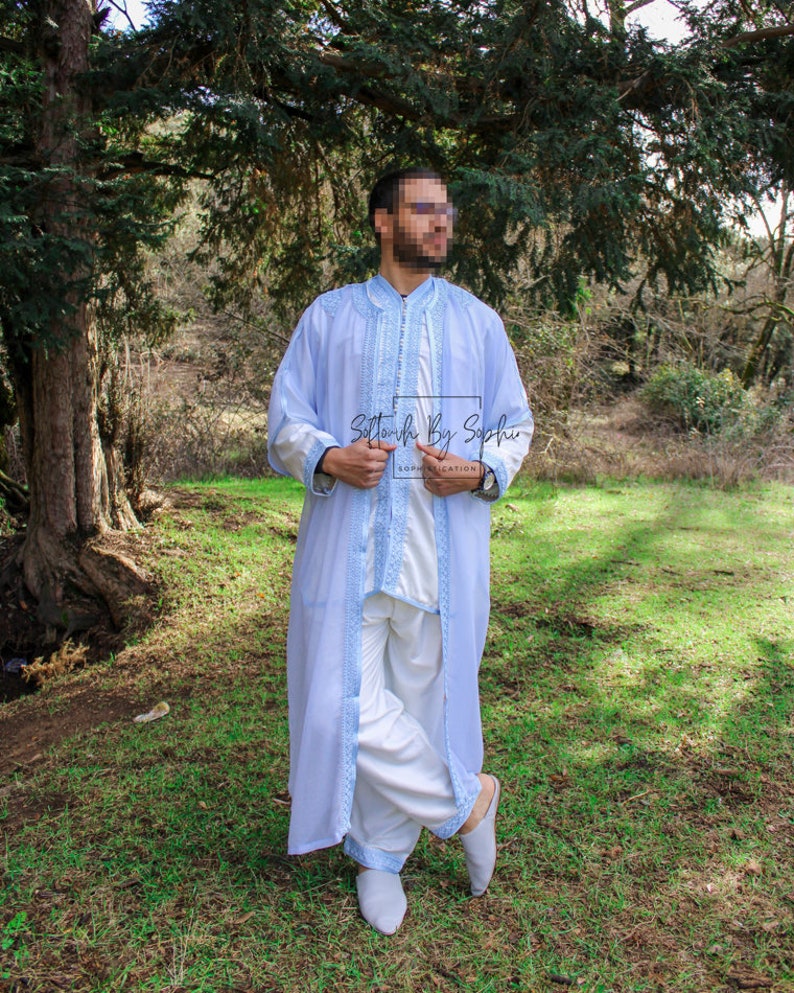 May include: A light blue robe with intricate embroidery and a matching white outfit. The robe features detailed light blue trim and embroidery along the edges. The outfit includes a long-sleeved top and loose-fitting pants. The text "Softouch By Sophie" is visible.