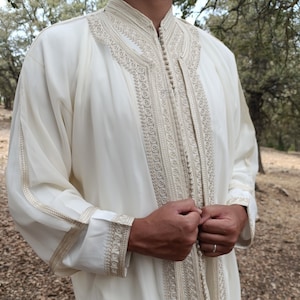 May include: A white long-sleeved robe with intricate gold embroidery around the collar, cuffs, and front closure. The robe is made of a lightweight fabric and has a relaxed fit.